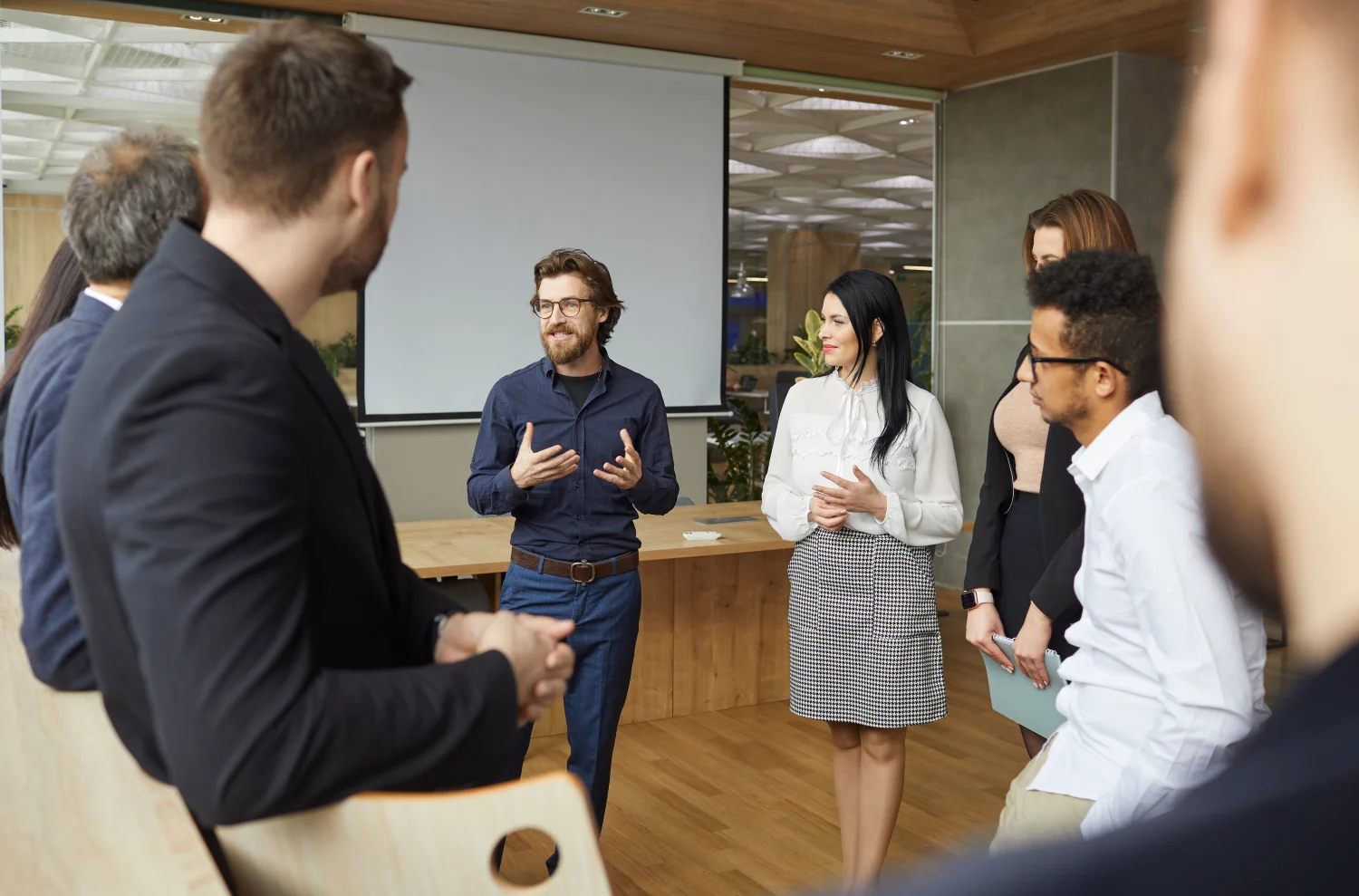 Business coach talking to group of people standing in office around him